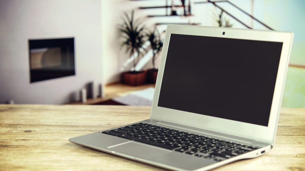 A budget laptop open on a wooden desk in a home living room