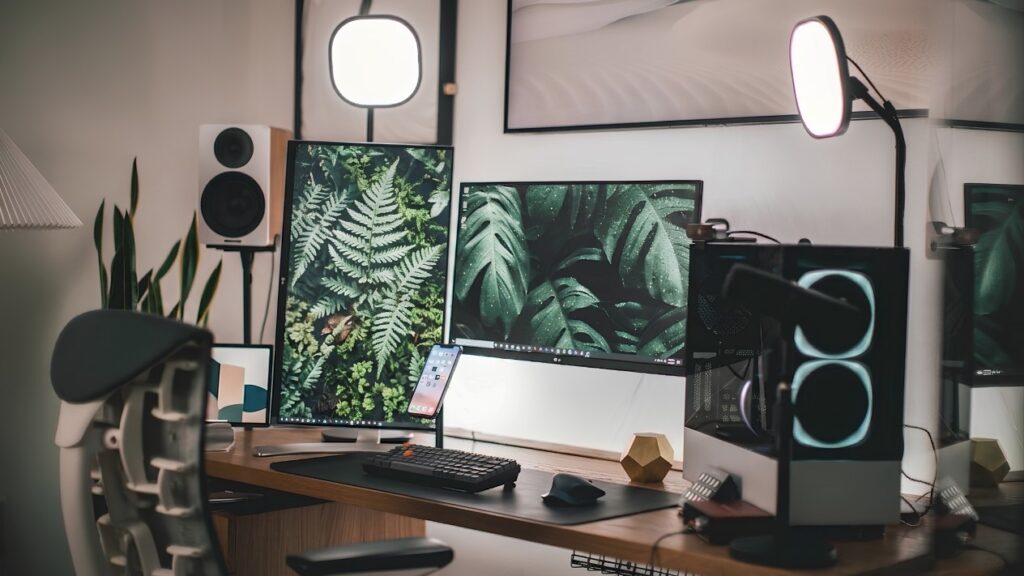 Desk setup with two monitors, a small PC case, studio lights and plants