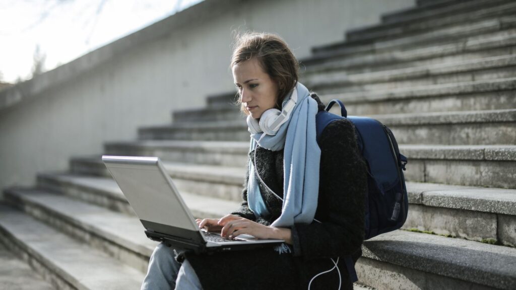 Student using a lightweight laptop outdoors on campus steps with a backpack