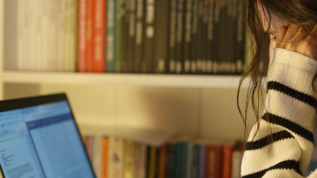 Student studying on a laptop at home with bookshelves behind
