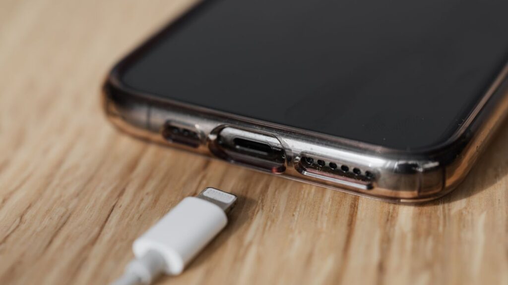 Close-up of a smartphone charging port with a Lightning cable lying unplugged beside it on a wooden surface