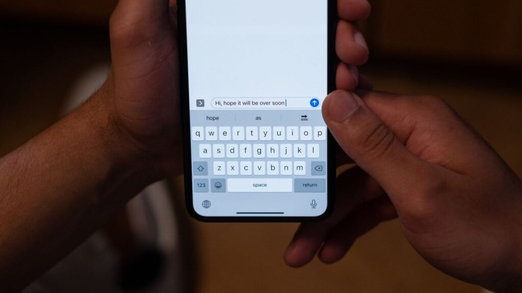 Hands holding an iPhone with the on-screen keyboard open mid-message, the part of the phone that holds the clipboard