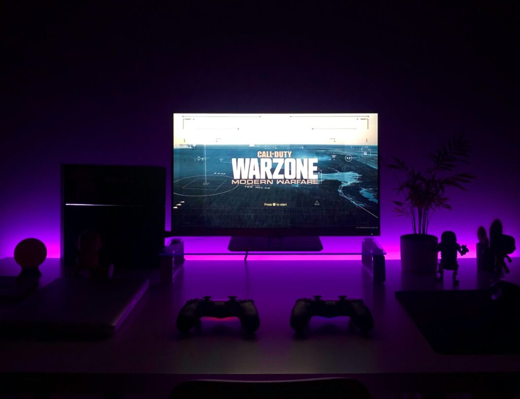 Games console and two controllers in front of a monitor running a game