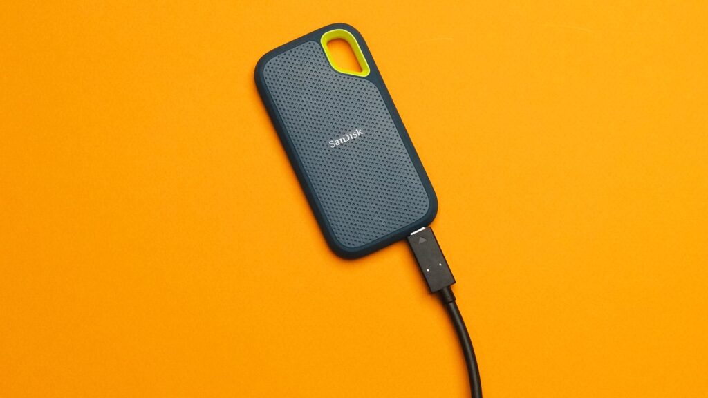 SanDisk portable external SSD with a USB-C cable on an orange background