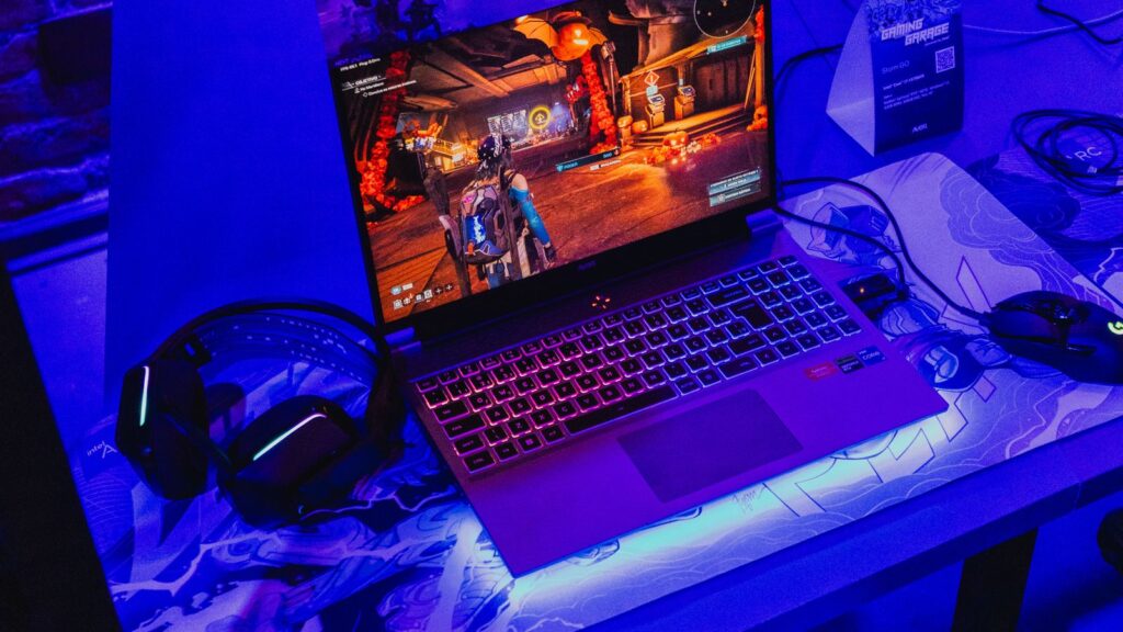 Gaming laptop with RGB keyboard running a game beside a headset and mouse