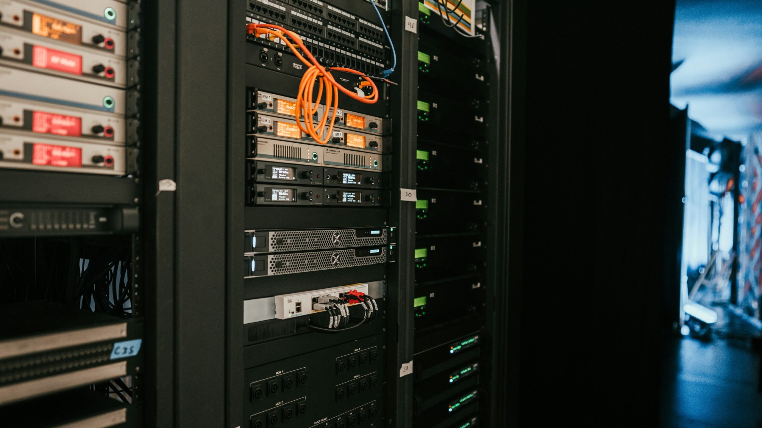 Racks of broadcast equipment with patch cables in a dim control room