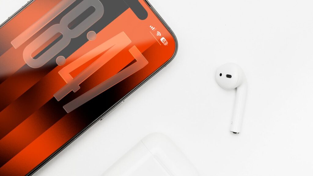 An iPhone with its display switched on next to an AirPod on a white surface