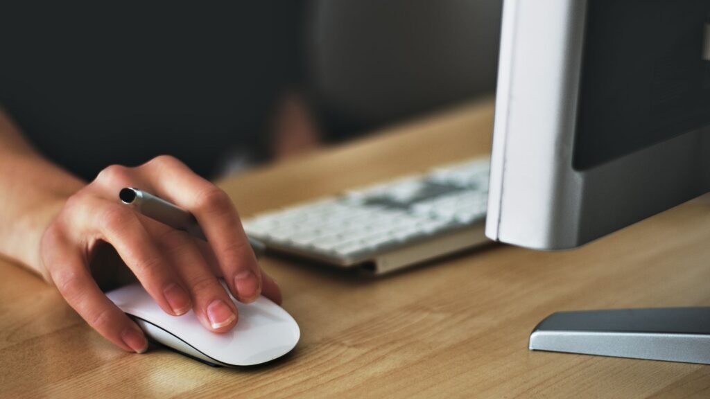 Hand resting on a wireless mouse at an office desk with keyboard and monitor