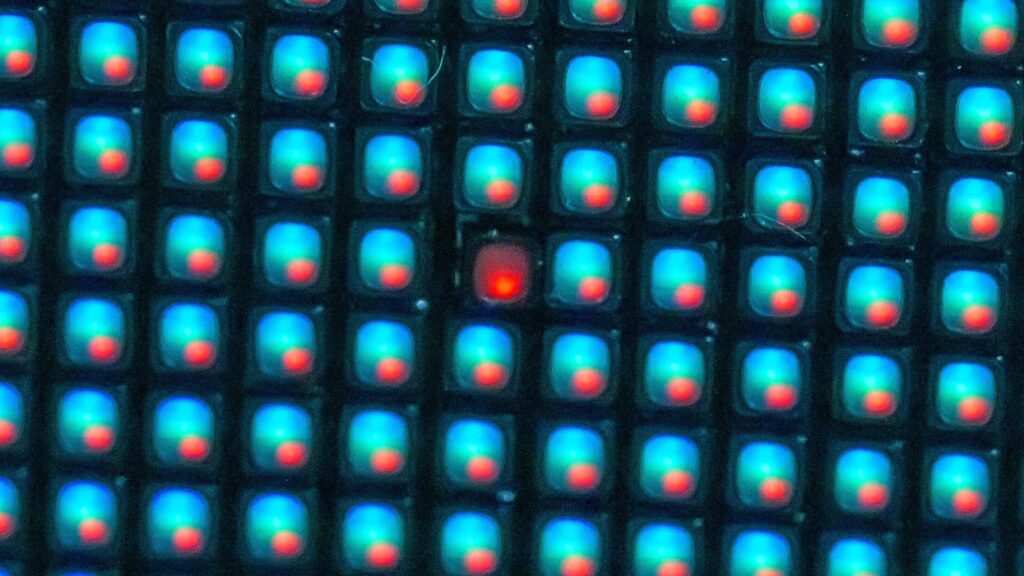 Close-up of a display pixel grid in which a single pixel is stuck showing red while every pixel around it works normally