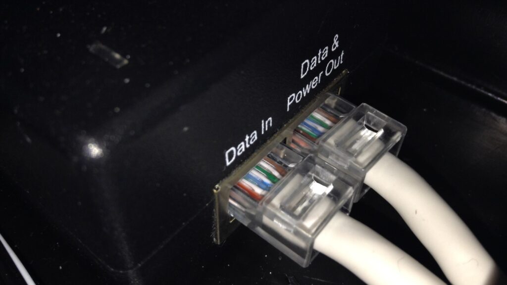 A Power over Ethernet injector with two network cables, one marked data in and one marked data and power out