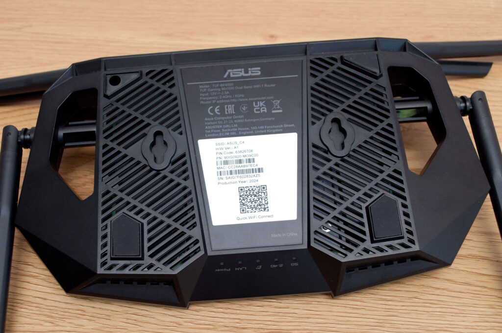 The underside of a WiFi router showing the sticker with default network name, password and QR code