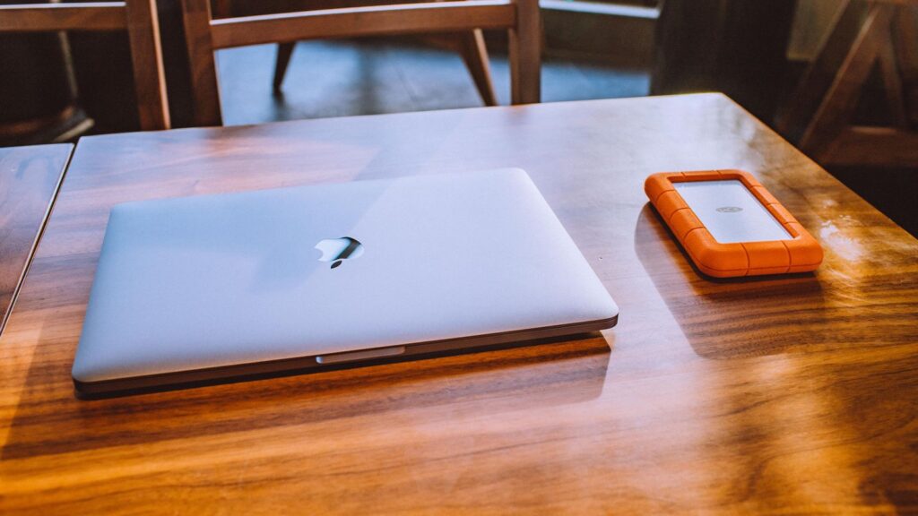 Rugged orange LaCie external hard drive next to a MacBook on a wooden desk