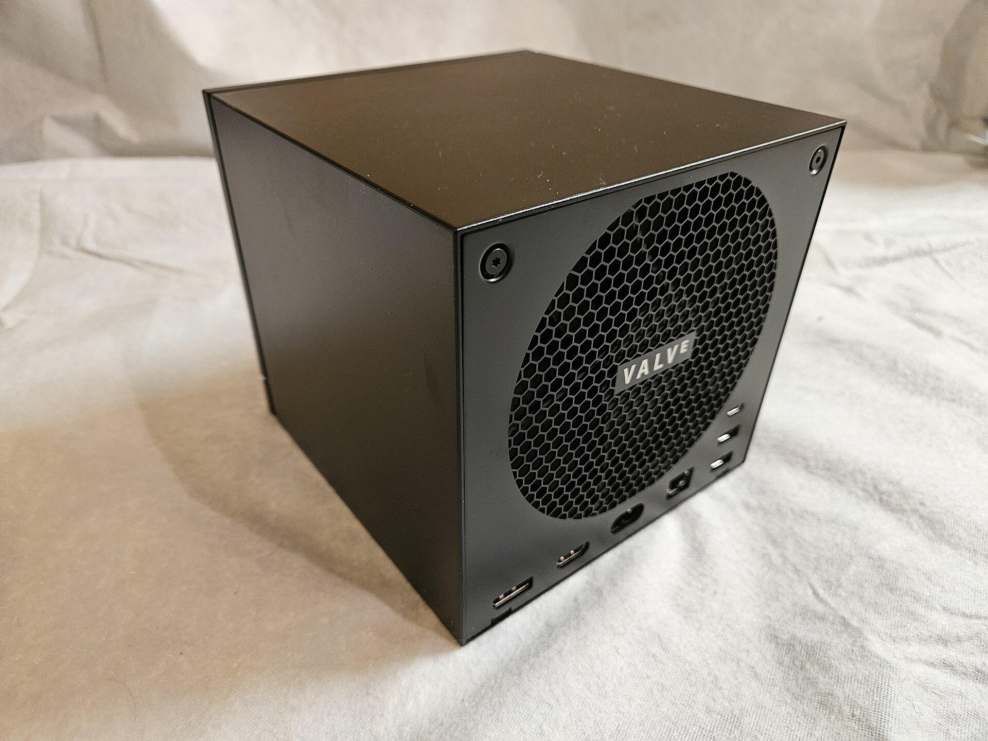 The Valve Steam Machine, a small matte black cube, showing the honeycomb rear fan grille with the Valve logo