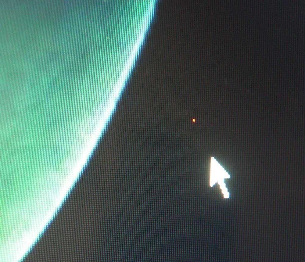 Close-up of a computer screen showing a stuck red subpixel as a tiny red dot next to the mouse cursor