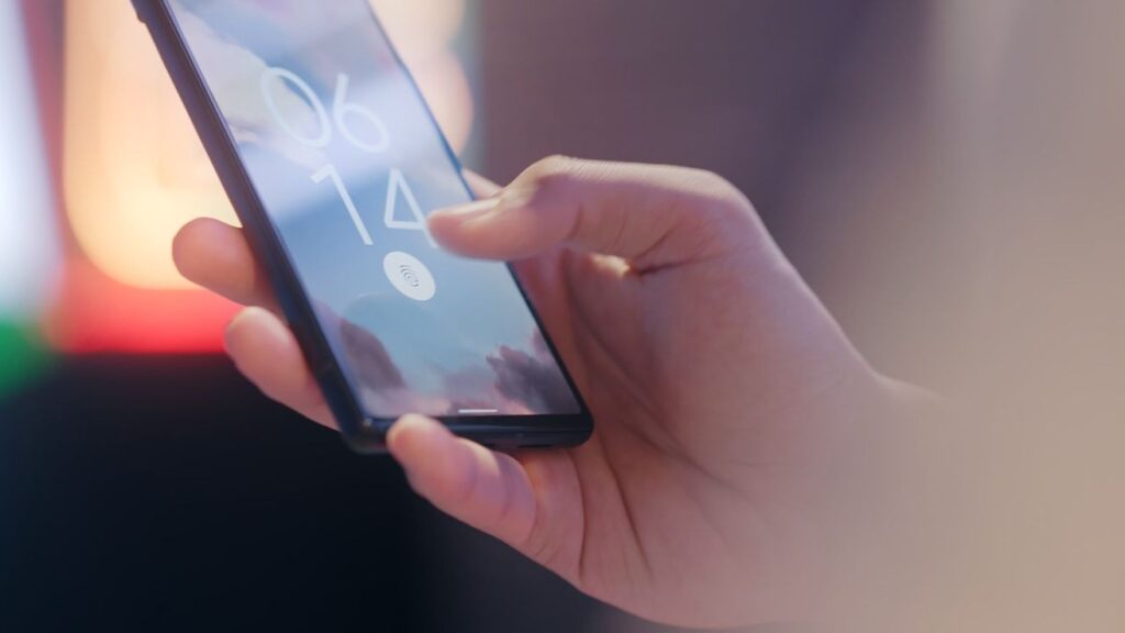 Hand holding a phone showing a lock screen with a fingerprint prompt