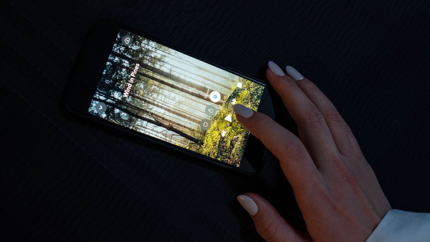 A hand reaching the screen of a phone lying on a dark surface