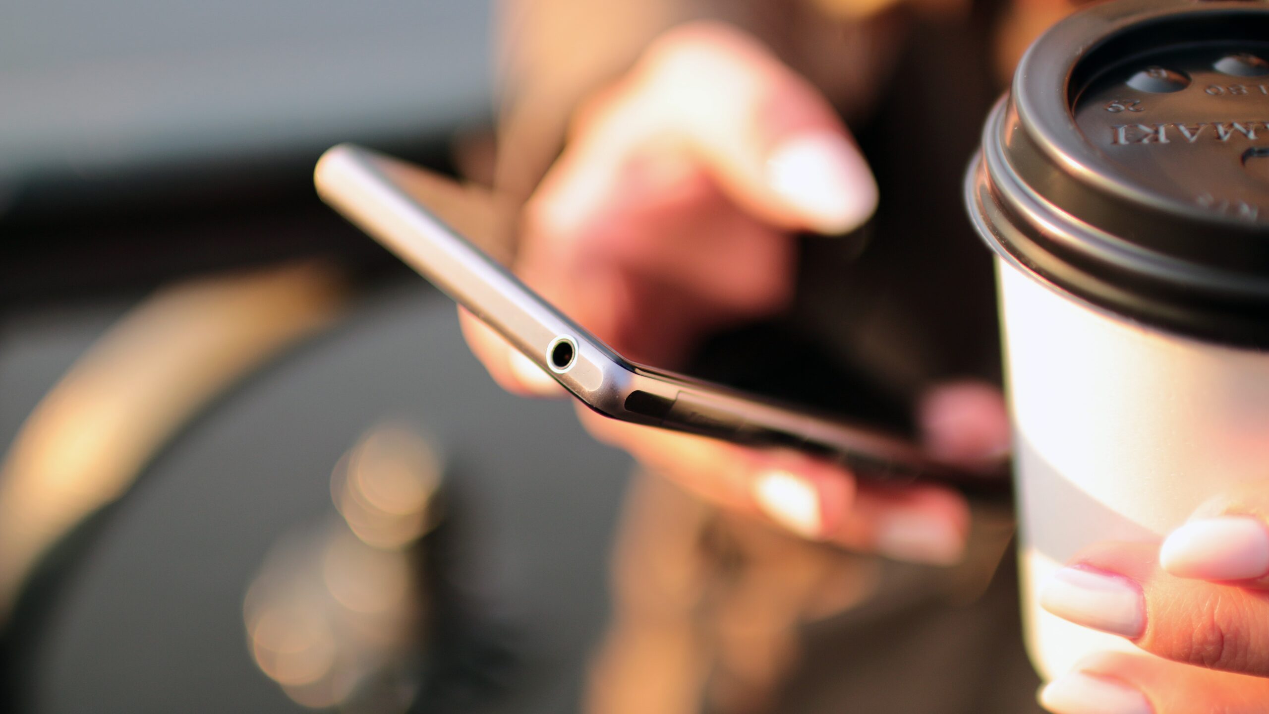 Hands using a smartphone next to a takeaway coffee cup