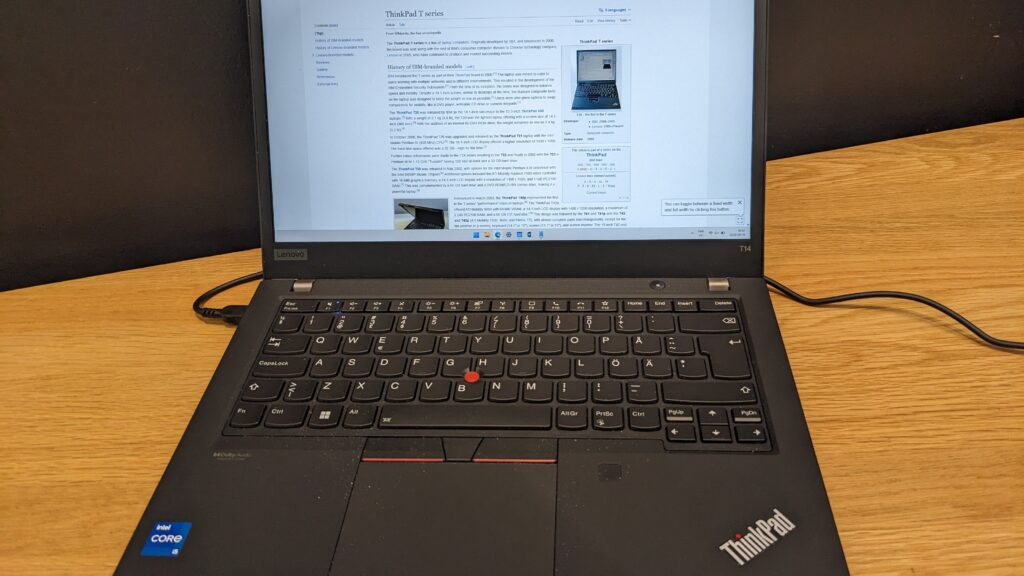 Lenovo ThinkPad T14 business laptop open on a wooden desk with a web page on screen