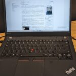 Lenovo ThinkPad T14 business laptop open on a wooden desk with a web page on screen