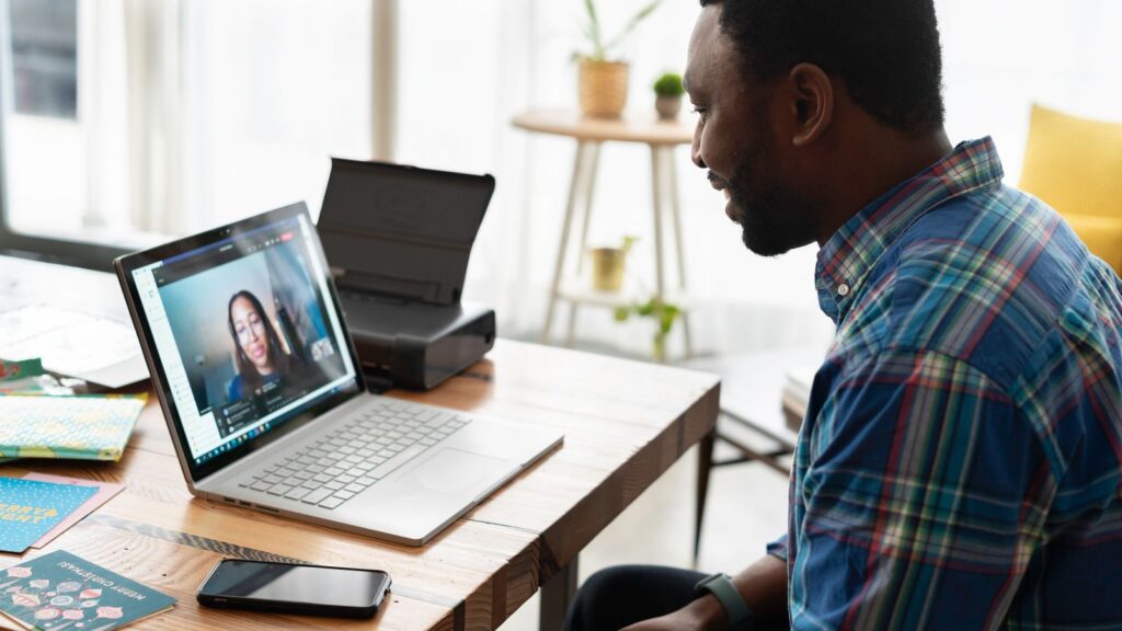 A man working on a laptop at a home desk with a wireless inkjet printer beside him