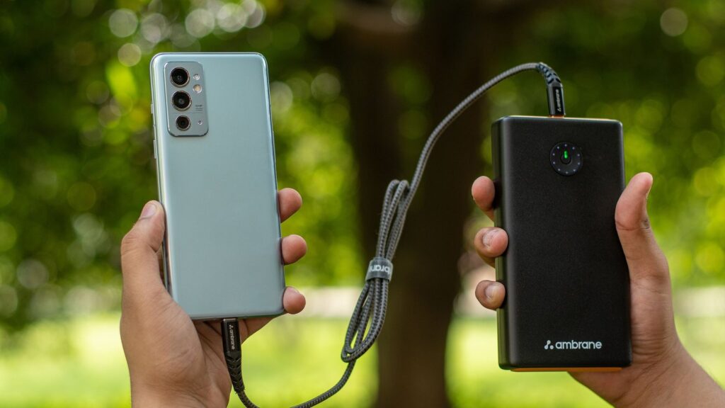 Two hands holding a smartphone connected by cable to a black power bank