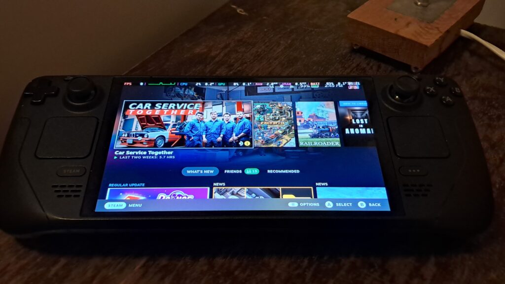 Steam Deck OLED on a table showing the SteamOS home screen with a performance overlay