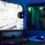 Curved gaming monitor next to a gaming PC with green lighting on a desk in a blue-lit room