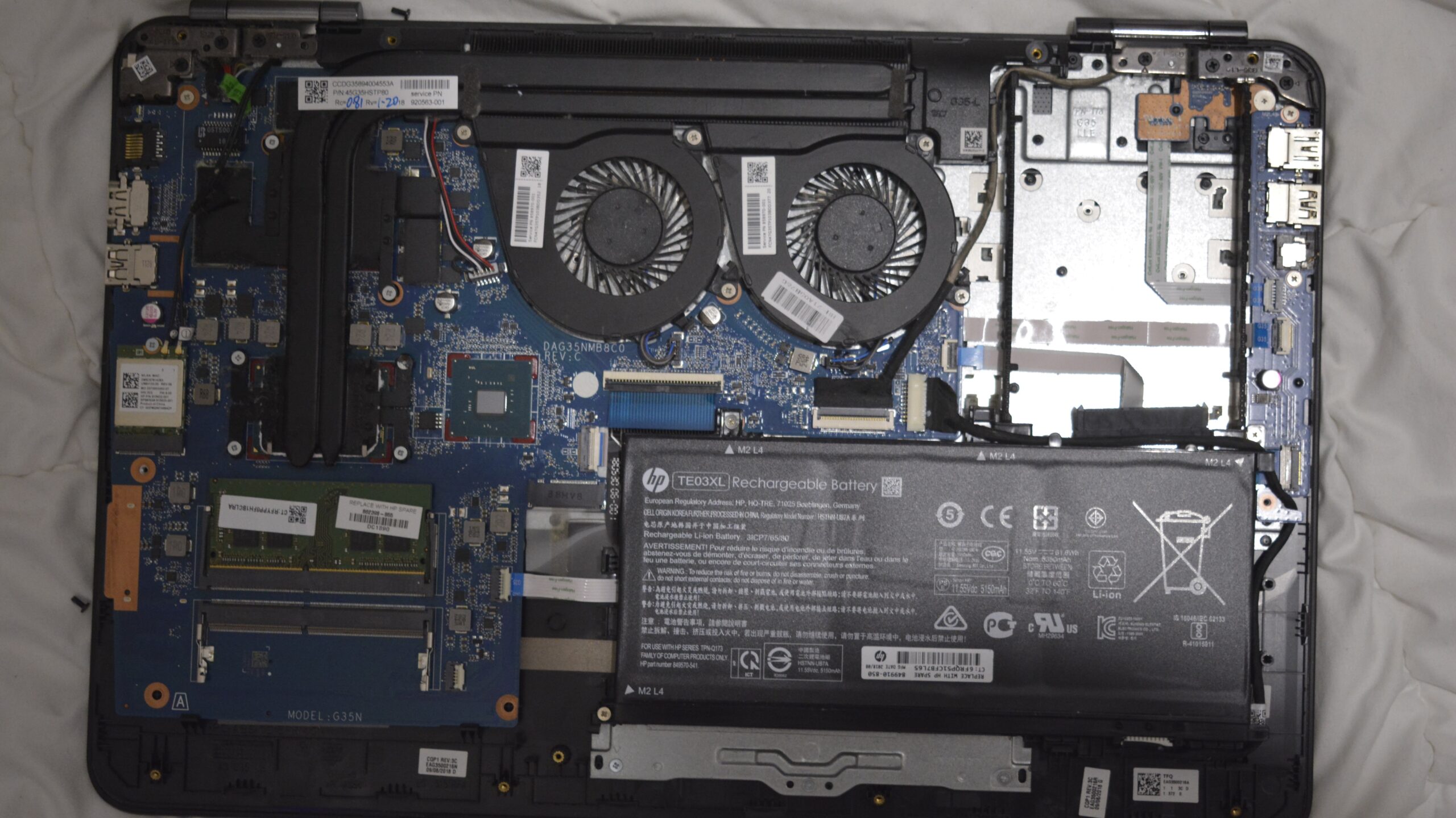 Inside an HP Pavilion 15 laptop with the base cover removed, showing the motherboard, cooling fans, battery and the two lid hinges