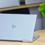 HP convertible laptop open on a wooden desk next to a green plant, seen from behind