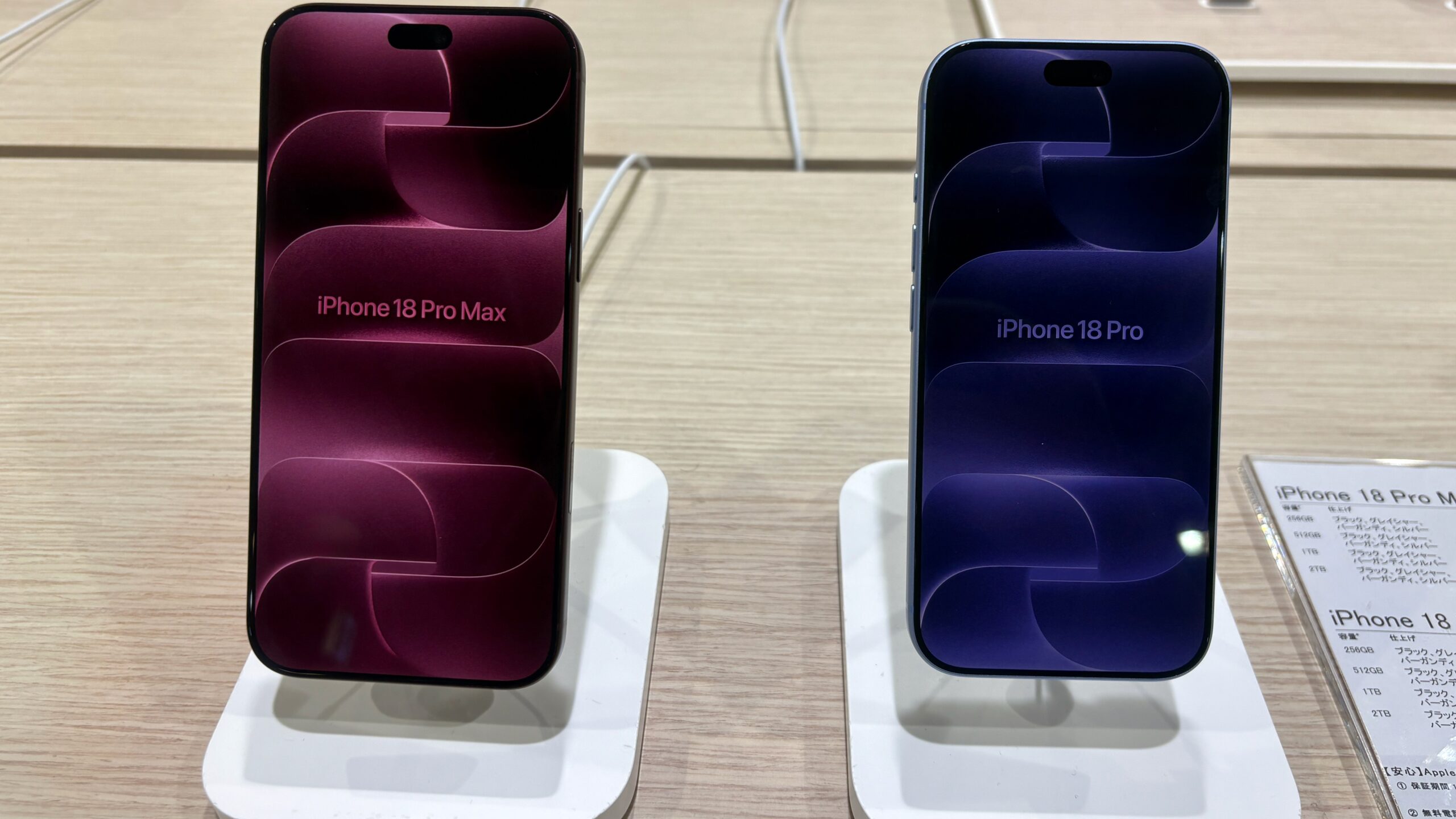 iPhone 18 Pro Max and iPhone 18 Pro standing side by side on a shop display, screens on