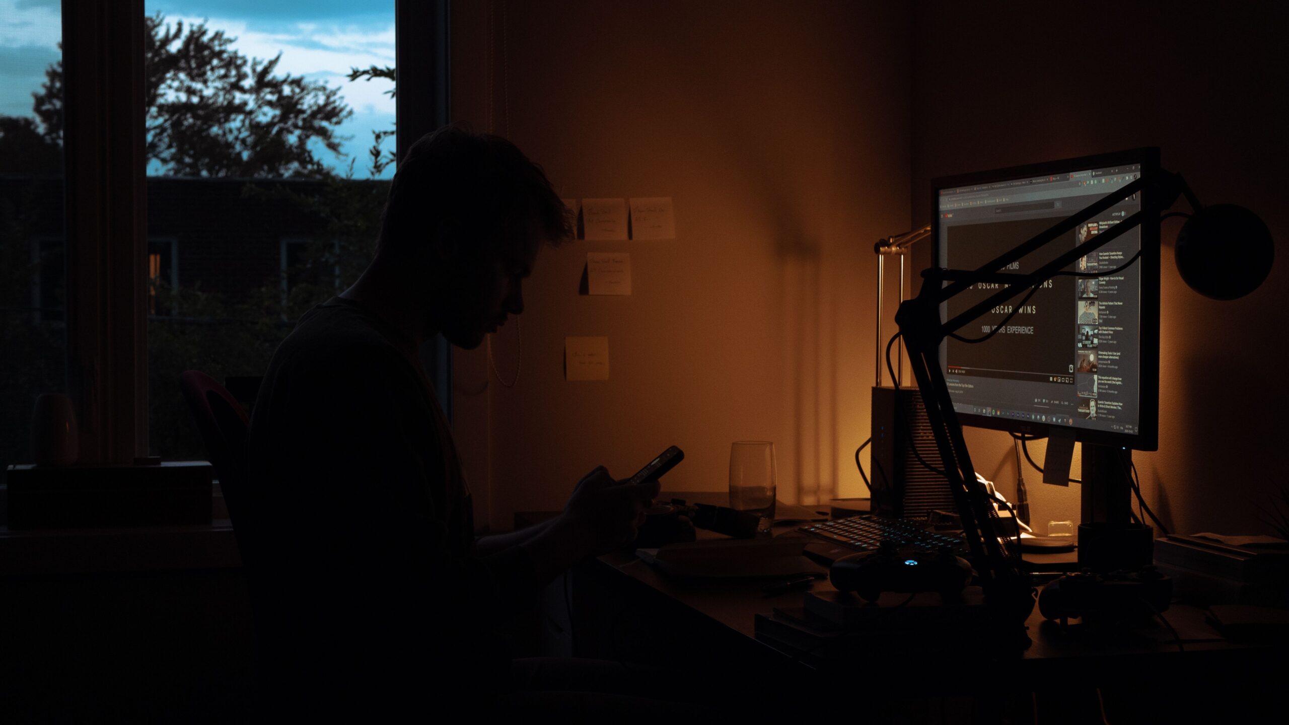 Person working at a computer monitor late at night in a dark room lit by a desk lamp