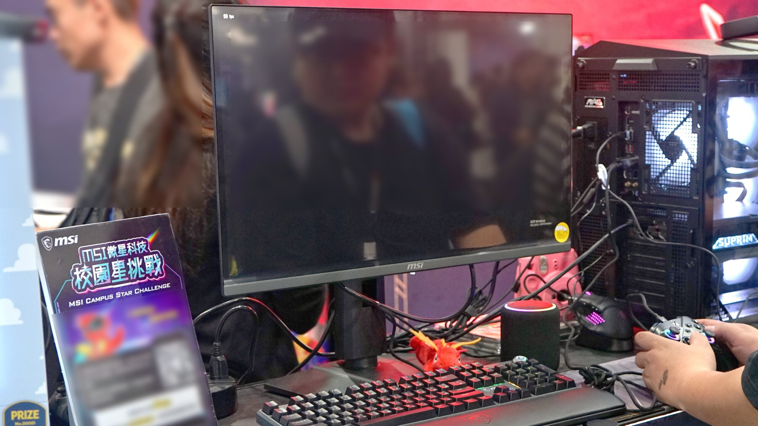 MSI MAG 272UP QD-OLED X24 gaming monitor on a stand at a gaming show, connected to a gaming PC