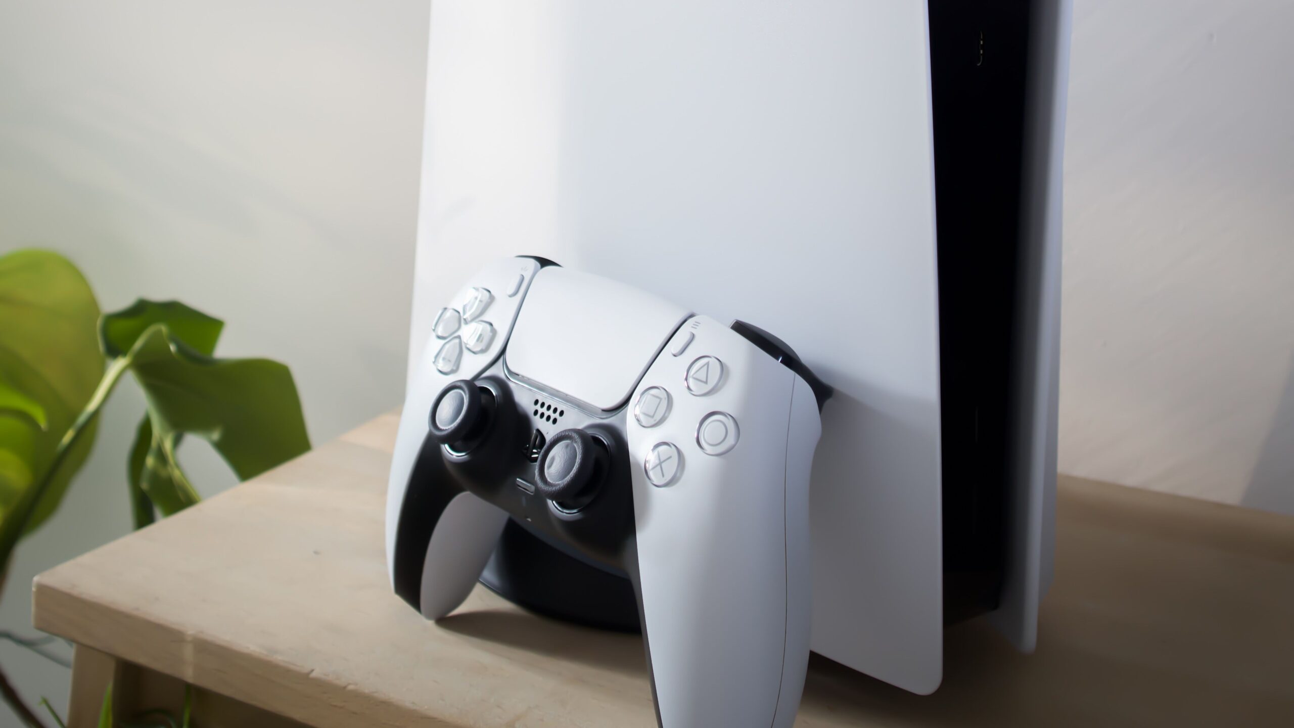 PlayStation 5 console standing upright with a white DualSense controller resting against it on a wooden table