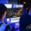 Gamers playing on a monitor at a PlayStation 5 gaming event with the PS5 logo above the screen