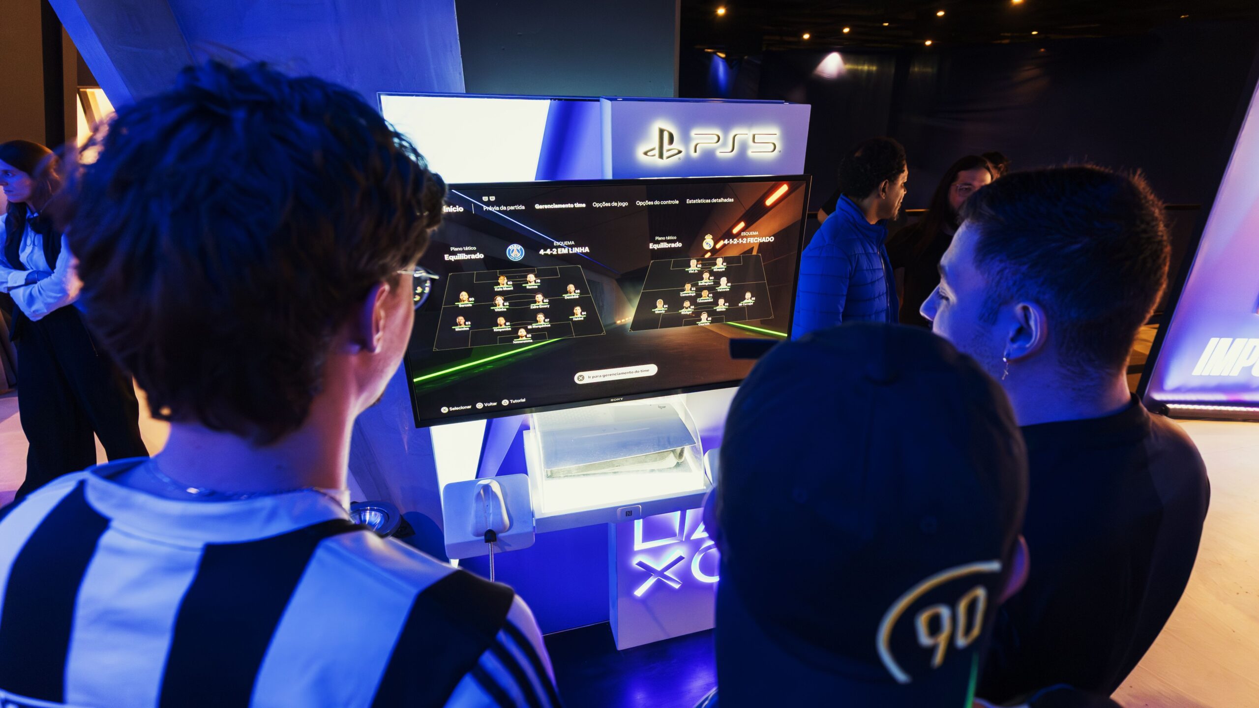 Gamers playing on a monitor at a PlayStation 5 gaming event with the PS5 logo above the screen