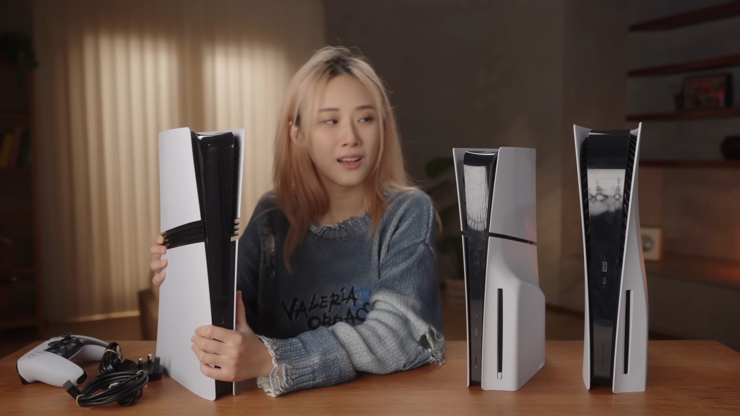 Three PlayStation 5 consoles side by side on a table: the PS5 Pro with three black stripes, the PS5 Slim and the original PS5