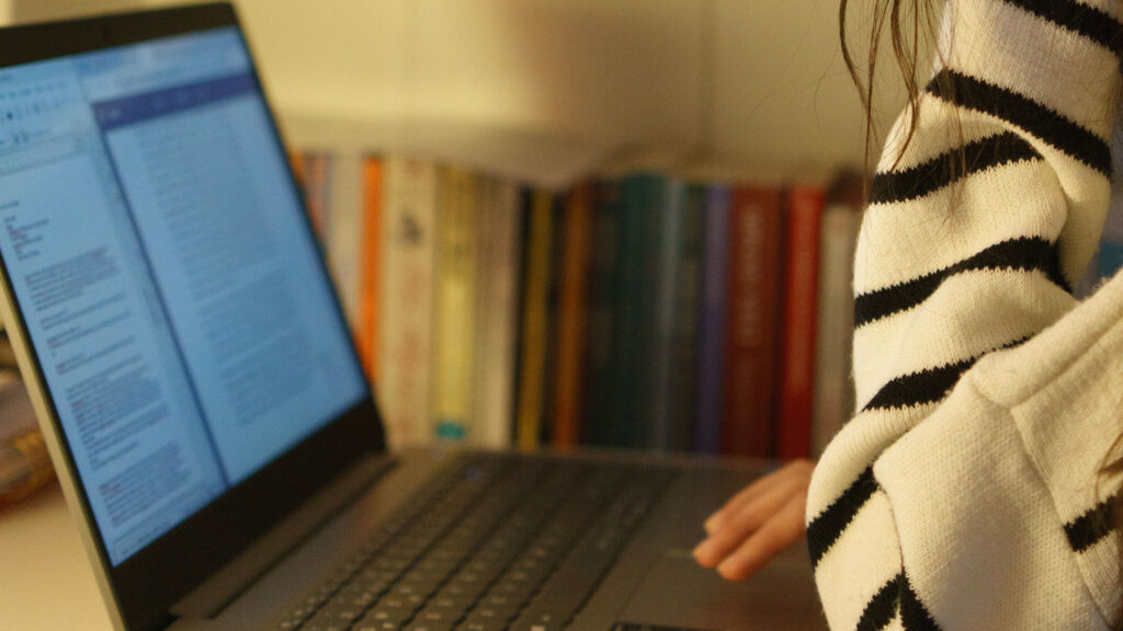 Student working on an essay on a laptop at a desk with books behind